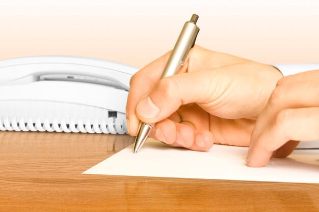 A person's hands carefully filling out a government form with a pen. The form is on a wooden desk.