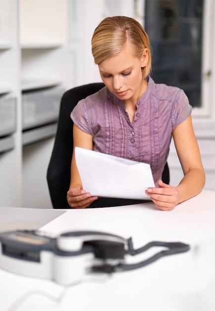 A person sitting at a desk, filling out an application form with a serious and focused expression. The desk is organized with papers, a pen, and a laptop, suggesting a deliberate and careful approach to the application process.