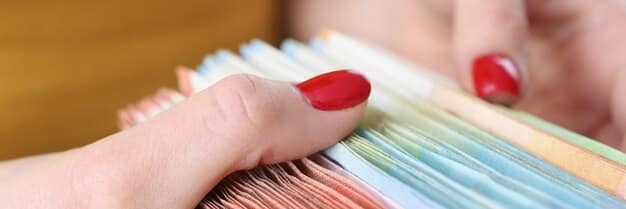 A close-up of hands carefully sorting through a stack of documents, with a calculator and pen nearby. The documents appear to be financial statements and income records, symbolizing the process of organizing and preparing income-related information for eligibility verification.
