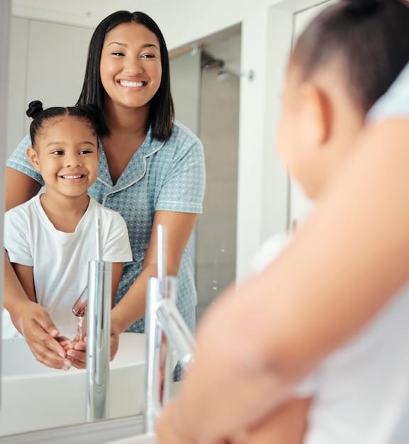 A close-up shot of a smiling mother dropping off her toddler at a bright and clean daycare facility, with a friendly caregiver greeting them at the door.